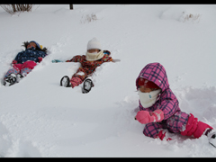 雪の布団に寝そべる園児3人